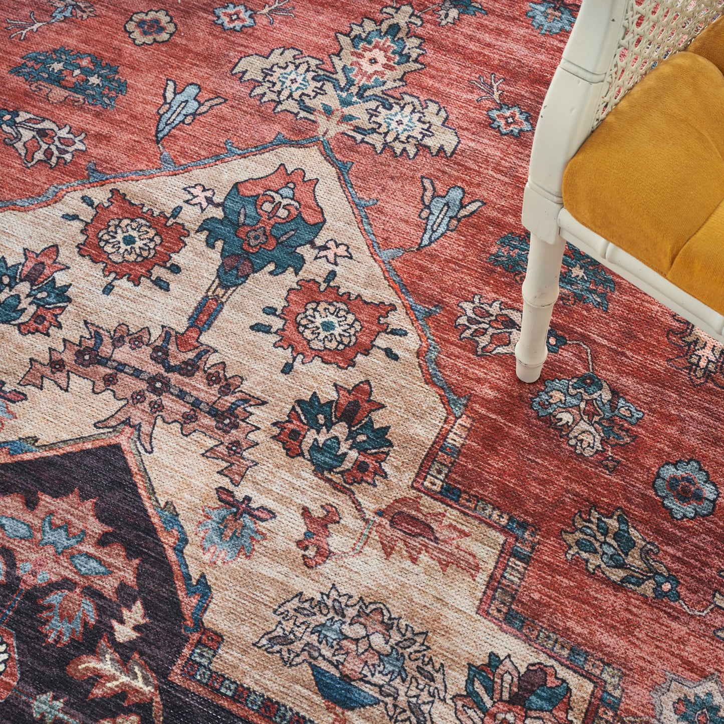 Persian-style red and cream area rug with blue floral motifs; white chair with a mustard yellow cushion visible.