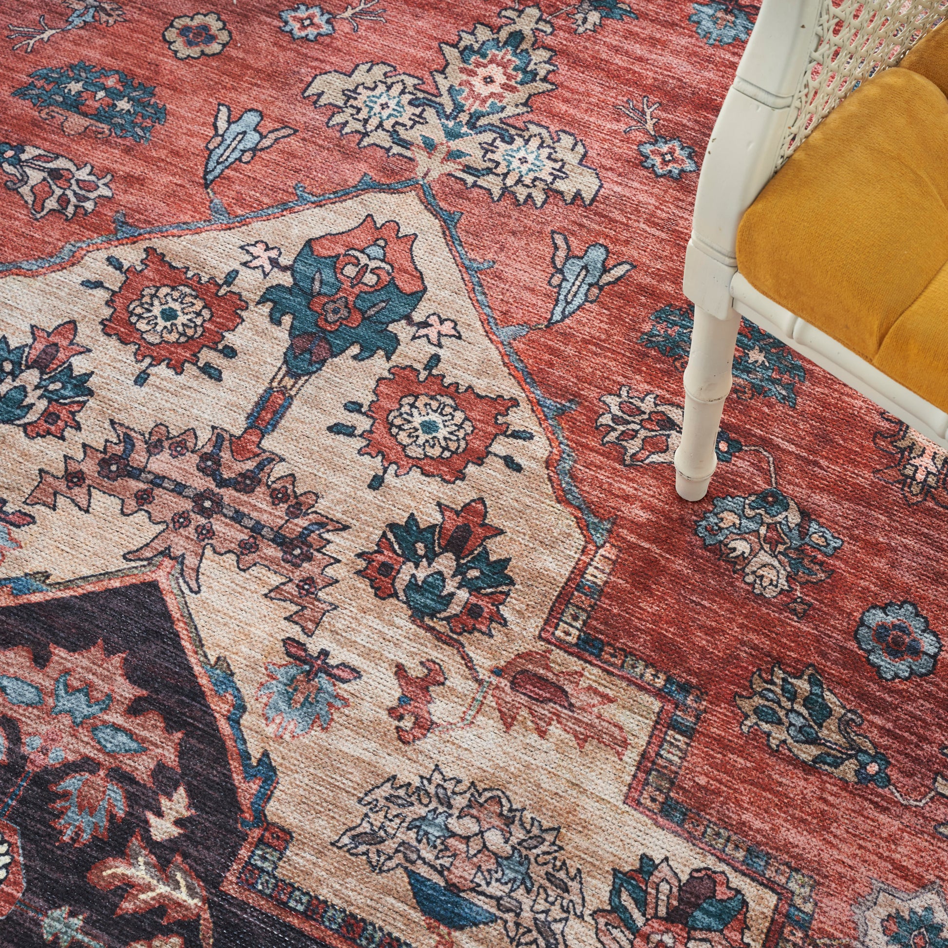Persian-style red and cream area rug with blue floral motifs; white chair with a mustard yellow cushion visible.