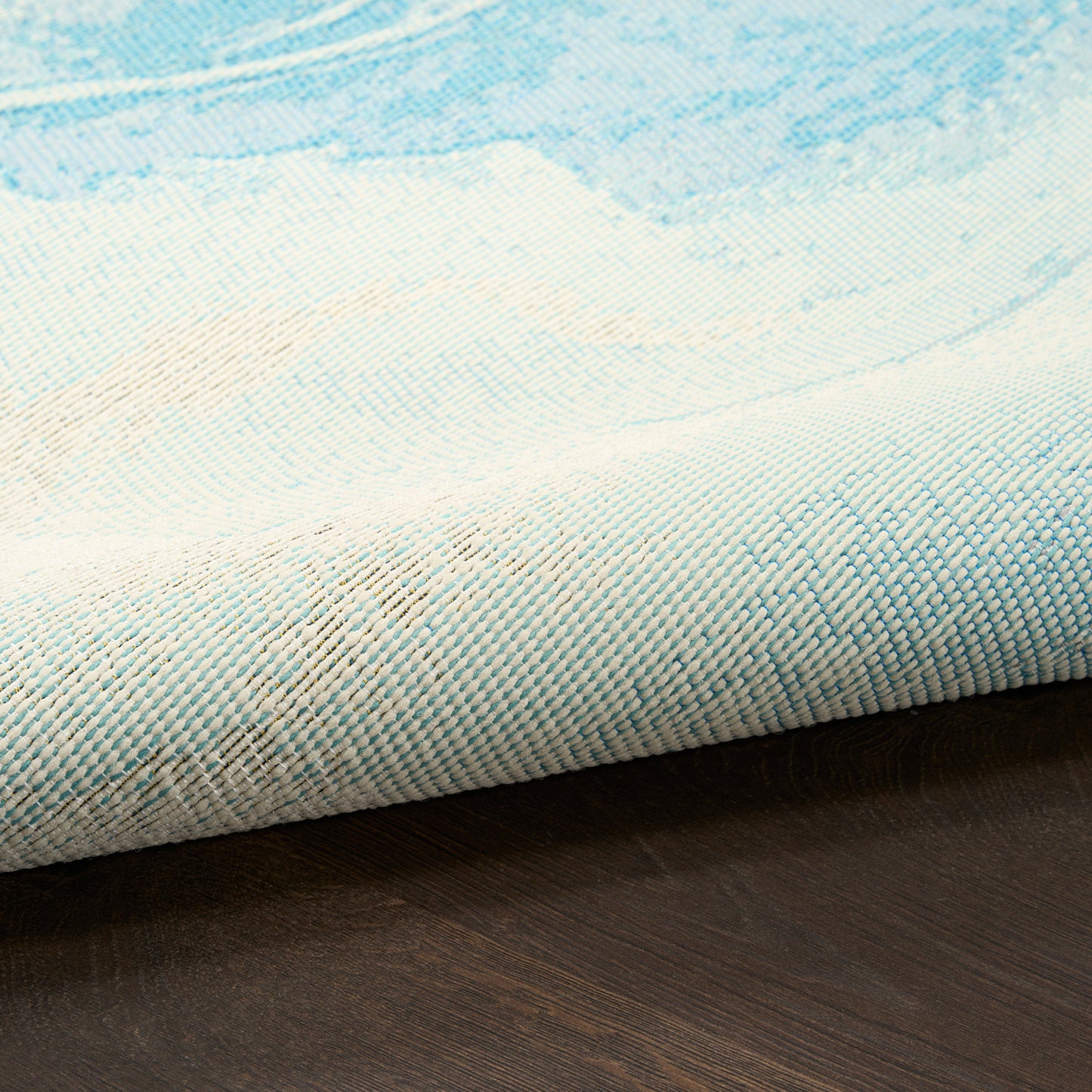 Blue & white woven rug with a soft watercolor pattern, rolled edge on dark wood floor, 8' x 10'.