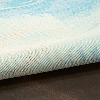 Blue & white woven rug with a soft watercolor pattern, rolled edge on dark wood floor, 8' x 10'.