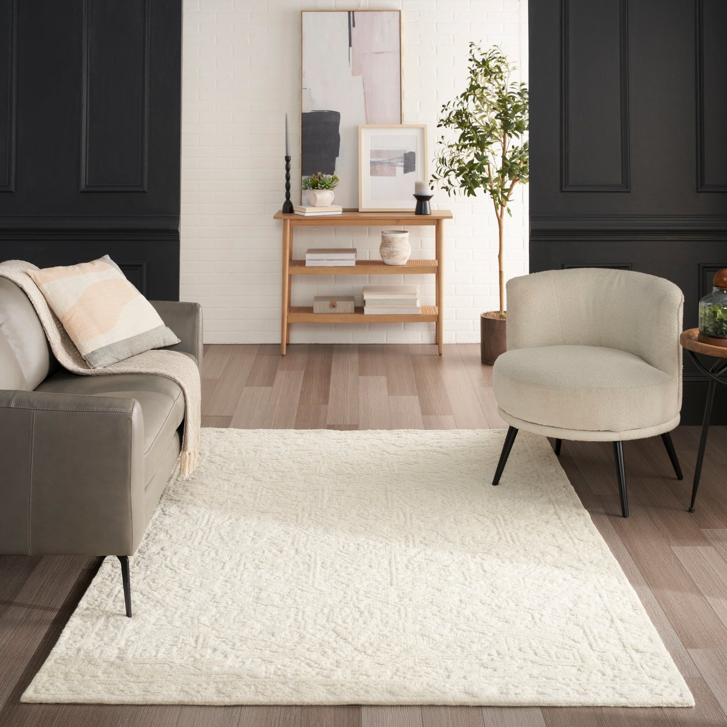 Cream textured area rug on light hardwood in a living room with grey sofa, beige chair, black paneled walls, and a console.