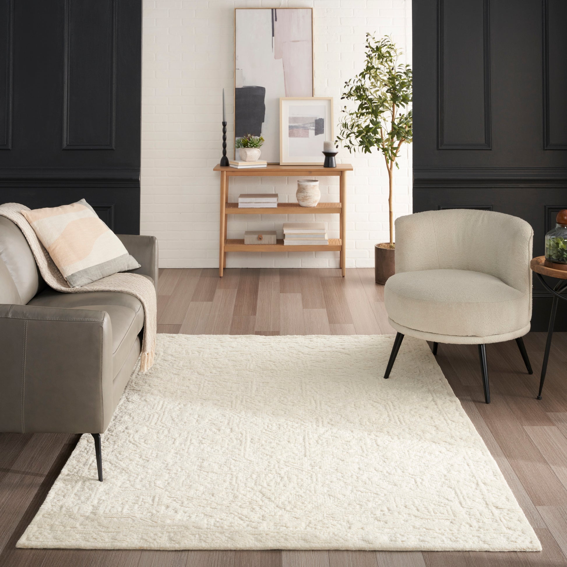 Cream textured area rug on light hardwood in a living room with grey sofa, beige chair, black paneled walls, and a console.