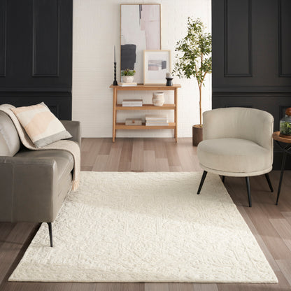 Cream textured area rug on light hardwood in a living room with grey sofa, beige chair, black paneled walls, and a console.