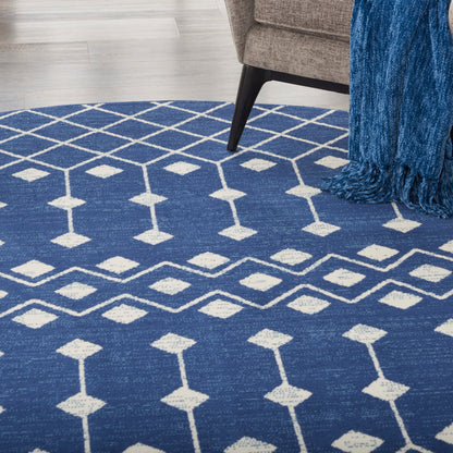 Blue geometric area rug with white diamond lattice pattern in a living room beside a sofa; blue fringed throw nearby.