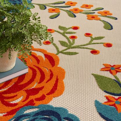 Beige woven area rug with vivid orange and blue floral pattern; potted fern rests on left edge.