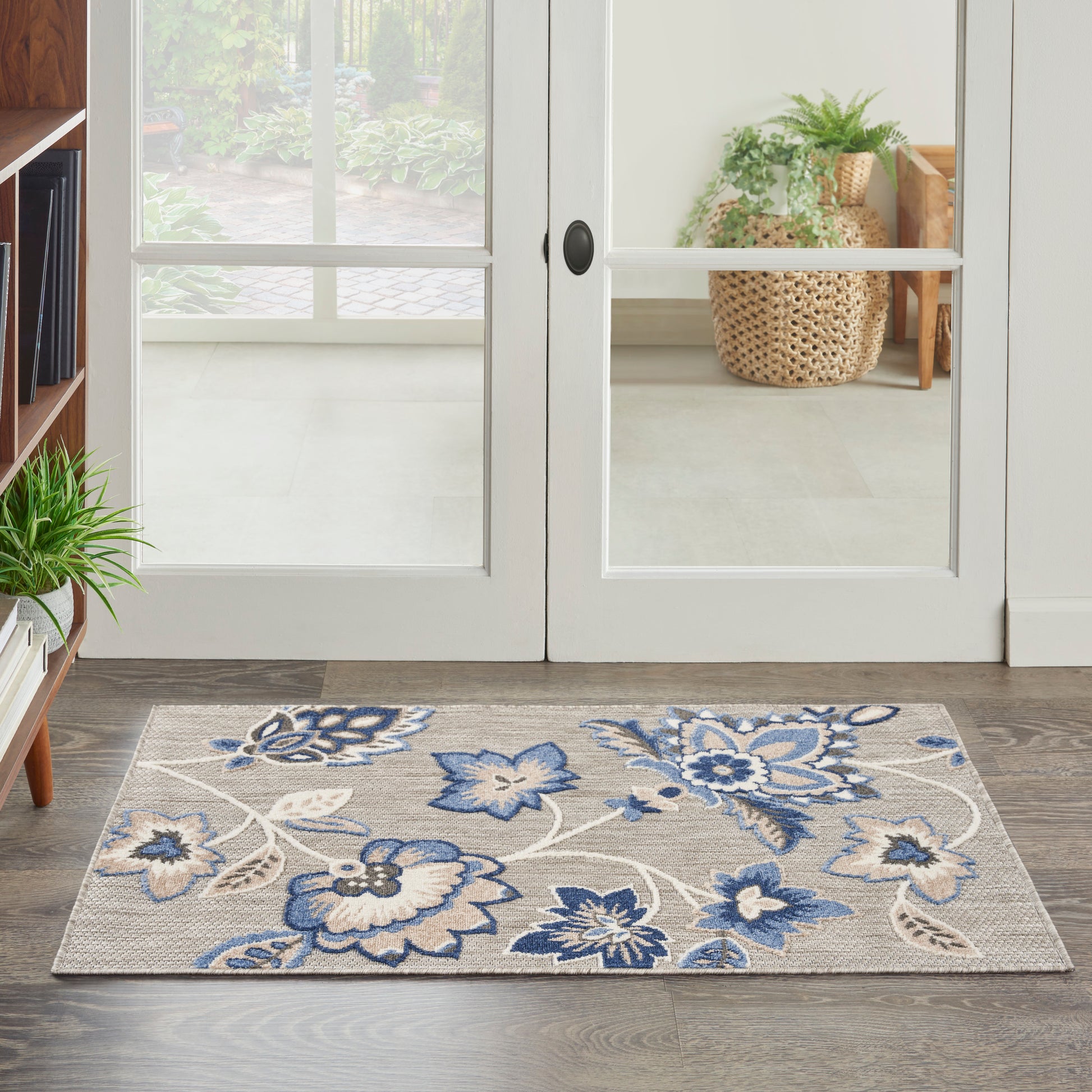 Beige rectangular area rug with blue floral motif on wooden floor beside glass French doors.