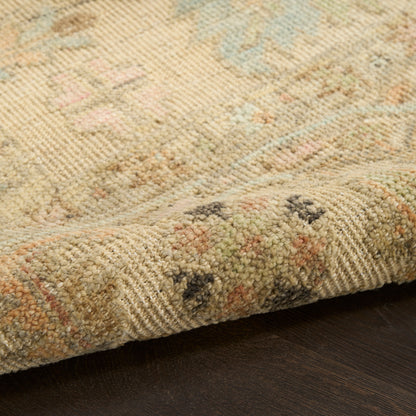 Beige woven rug with pastel blue, pink & green floral motif; folded edge on dark wood floor.