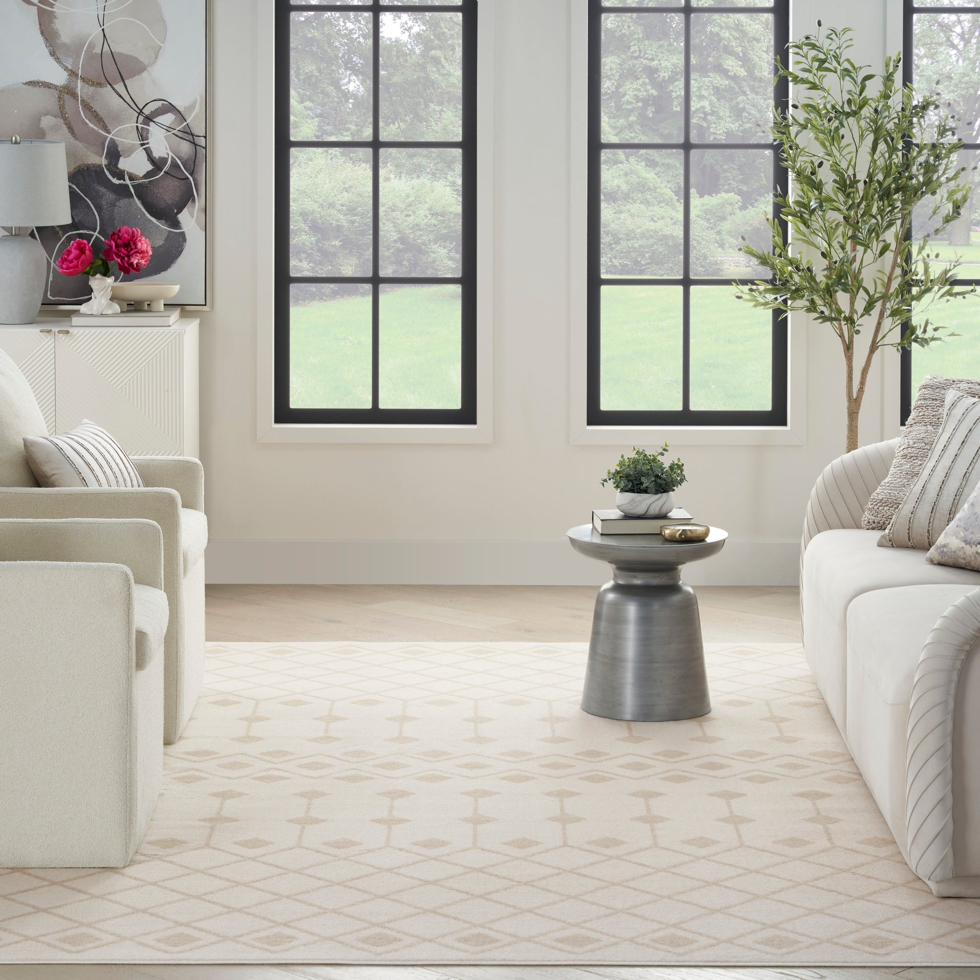 Bright living room with cream sofas, geometric beige rug, round metal side table, potted plants, and large grid windows.