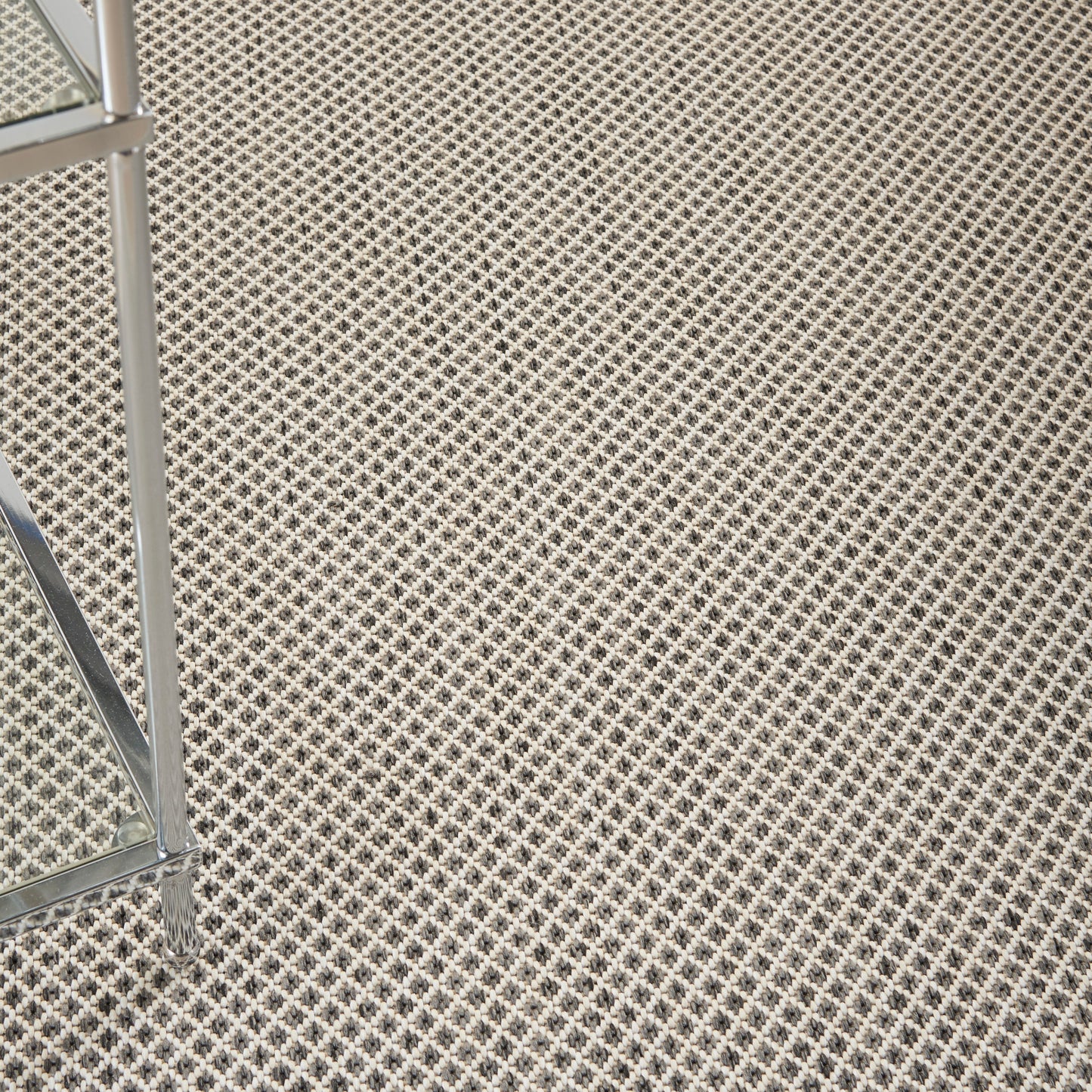 Beige diamond-pattern rug with a chrome chair leg on the left and a solid grey square patch.