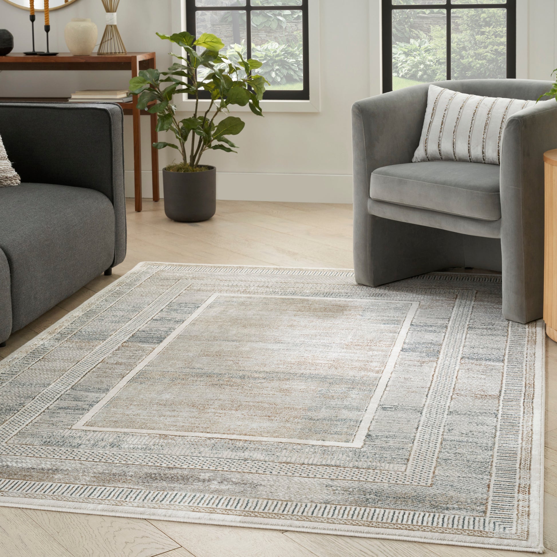 Light gray area rug with geometric border on wood floor, paired with grey sofa, armchair, and plant.
