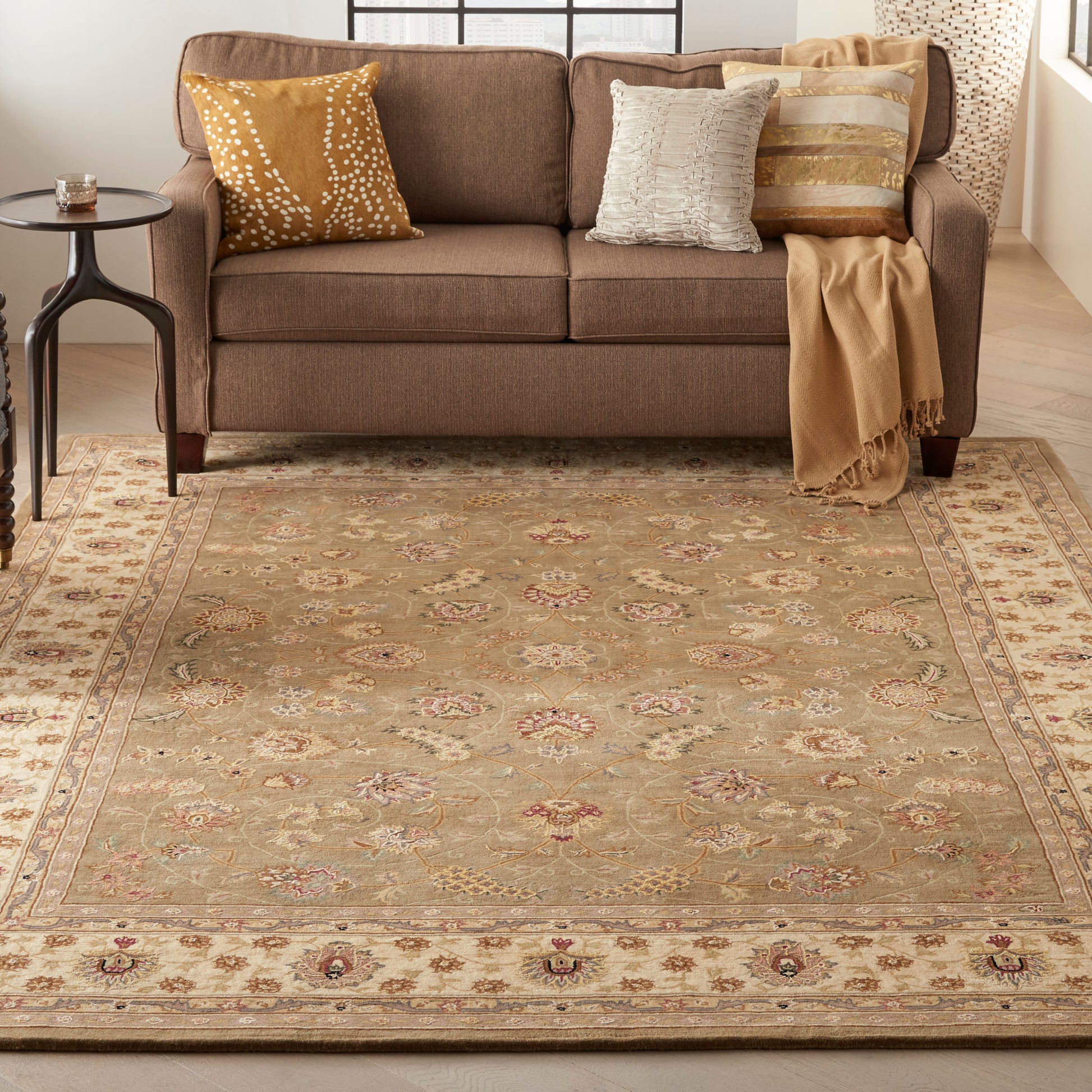 Brown fabric sofa with mustard and cream pillows, a camel throw, on a beige oriental rug in a cozy living room.