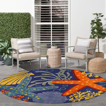 Round outdoor rug with navy base and colorful starfish and seaweed motif; beige patio chairs and woven side table.