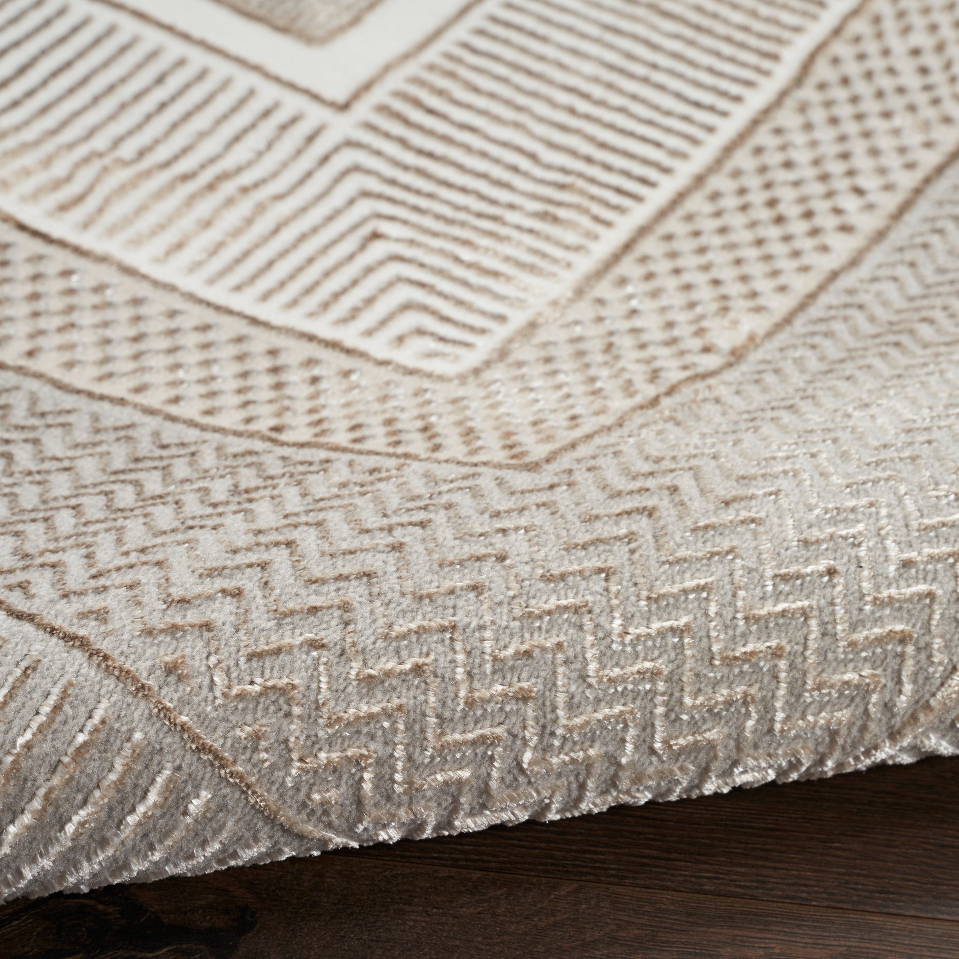 Beige textured area rug with layered geometric chevron patterns on dark wood floor.