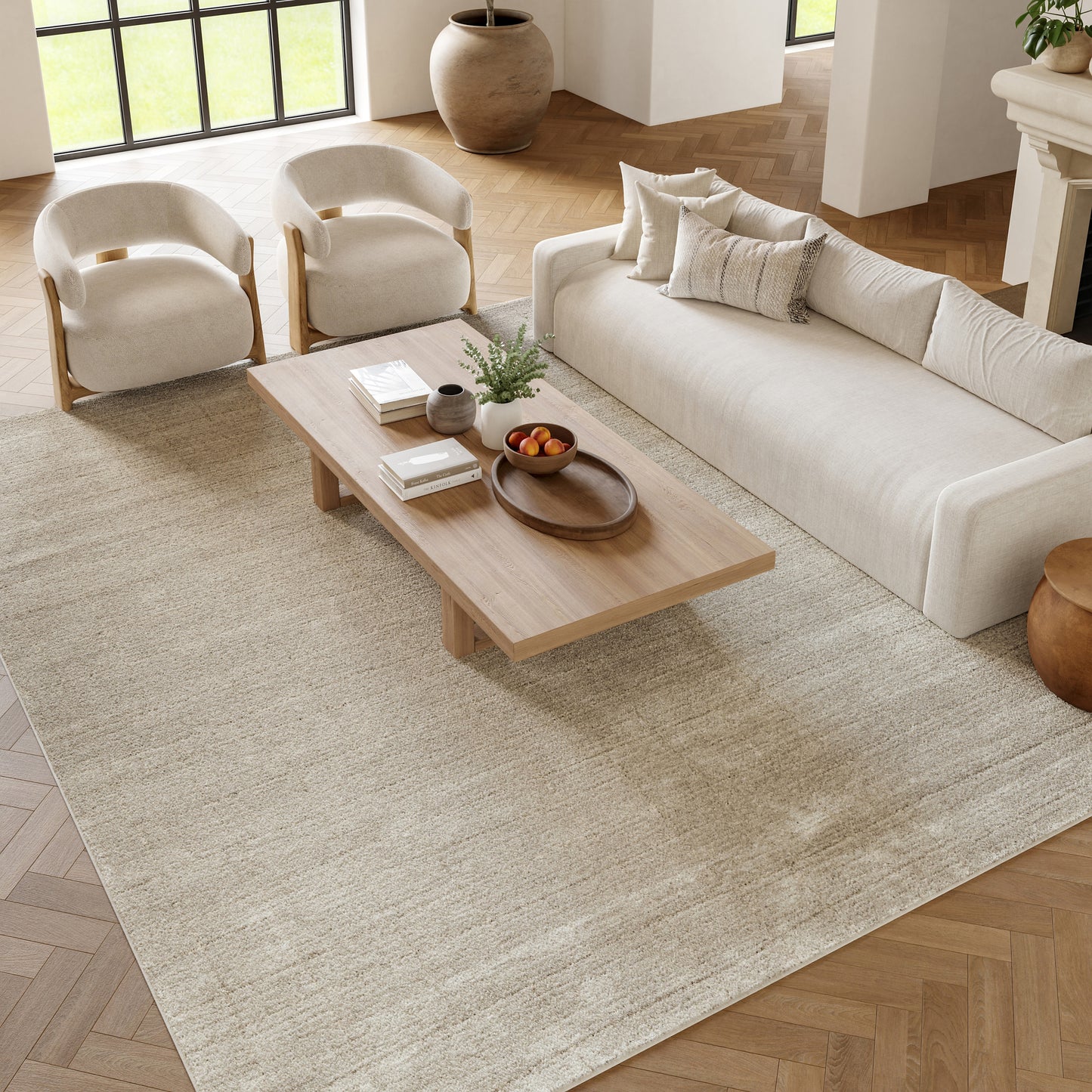 Bright modern living room with beige sofa, two cream wood-framed armchairs, a low wooden coffee table on a neutral rug.