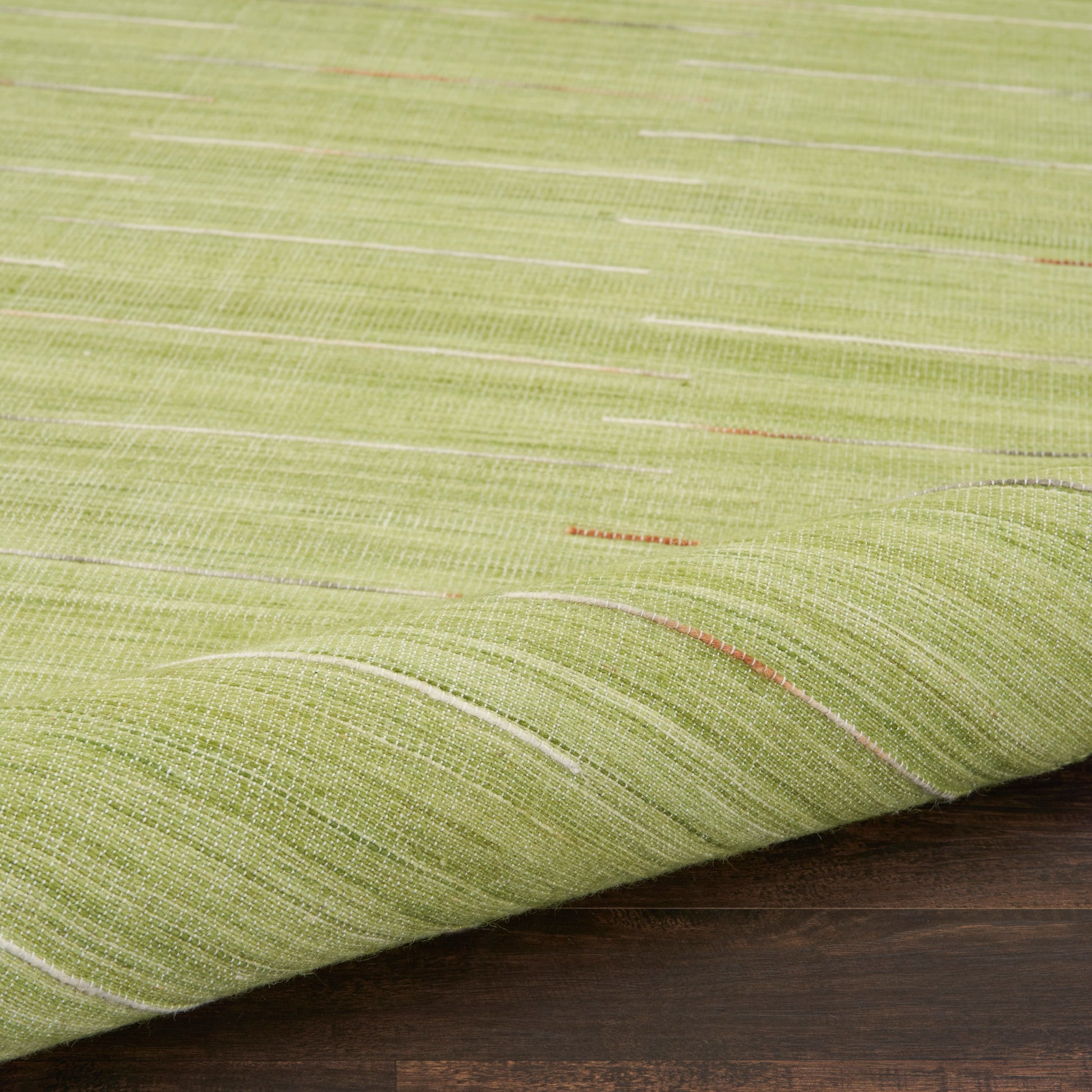 Close-up of lime-green woven rug with white and orange threads, rolled edge on dark wood floor.
