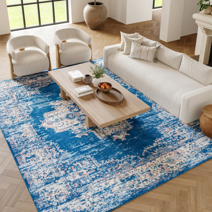 Living room with blue distressed rug, beige sofa, two cream curved armchairs, and light wood coffee table.