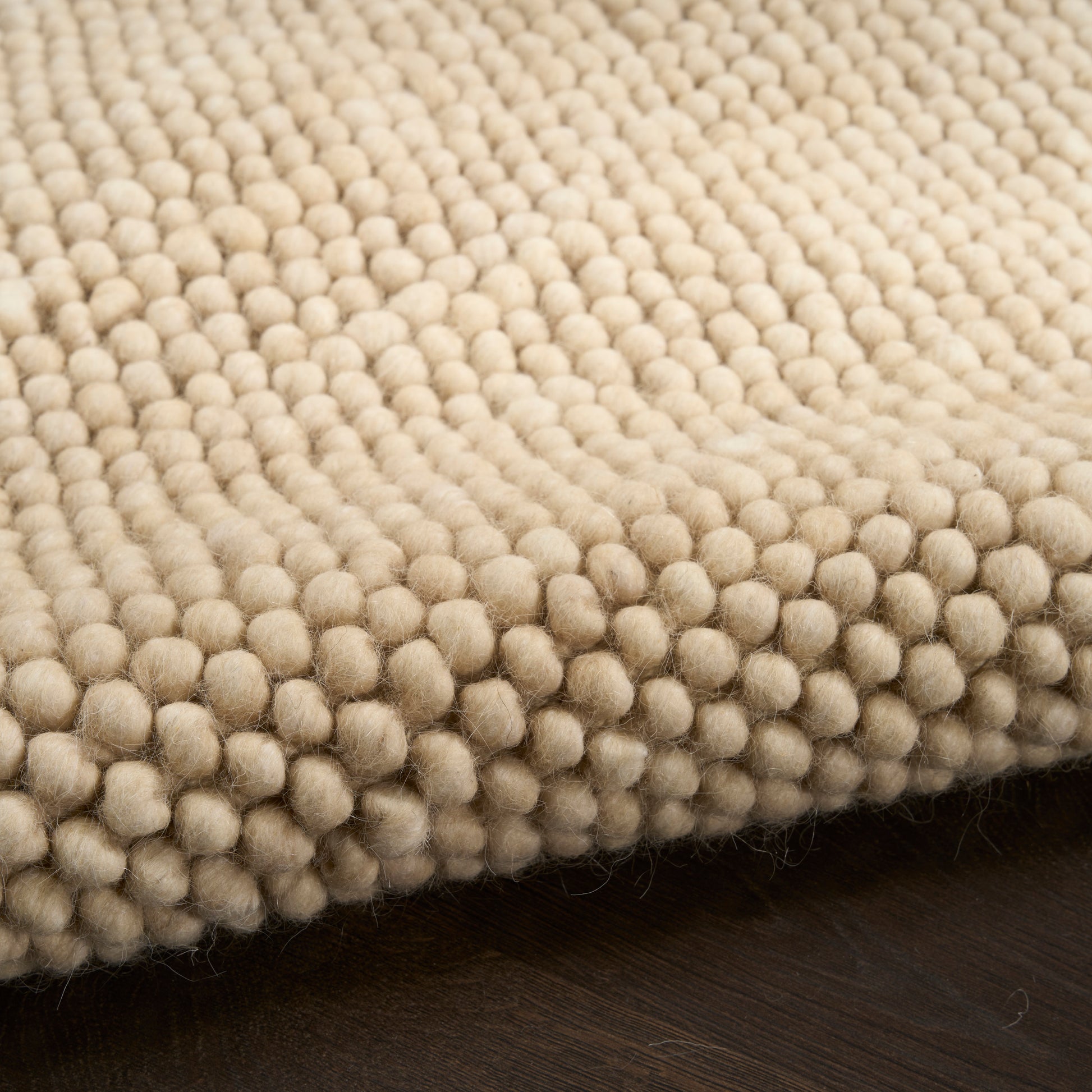 Cream boucle rug with dense, round tufted bobbles on dark wood floor.