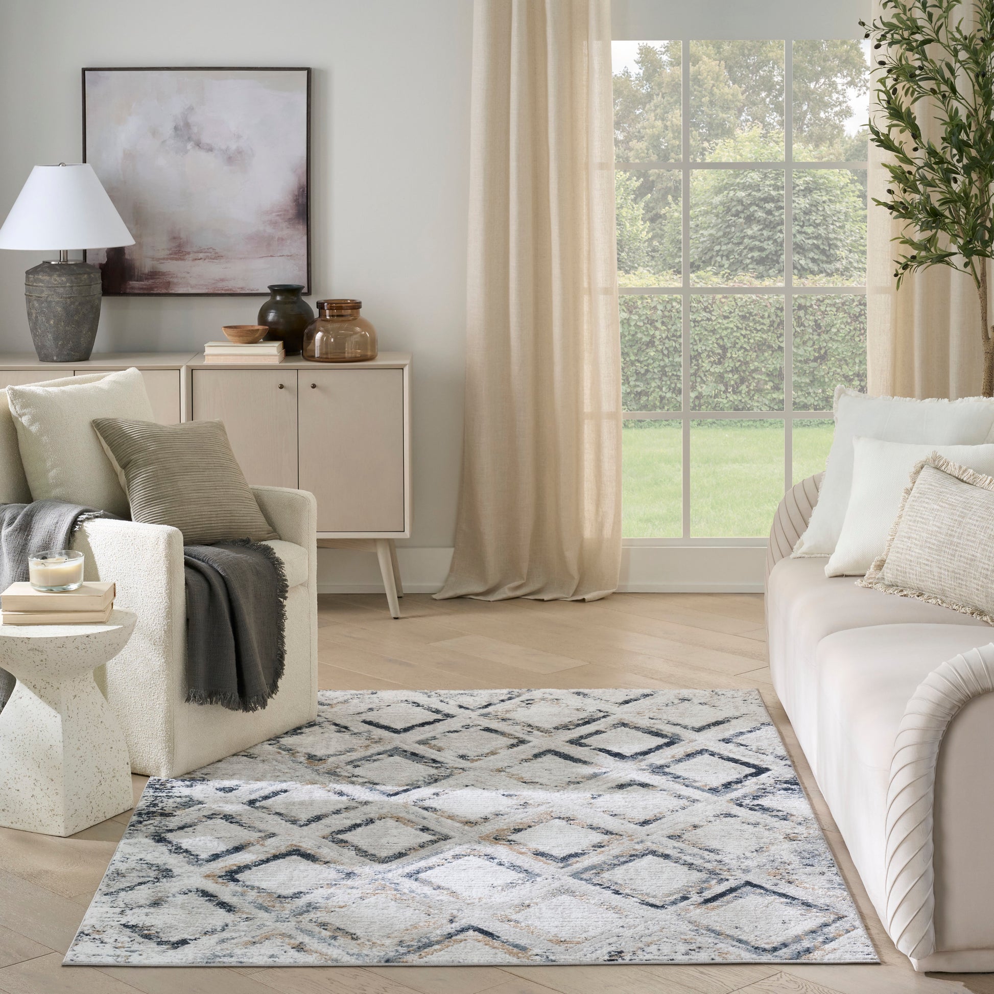 Neutral living room with cream sofa, textured throw, blue-gray diamond-pattern rug, beige drapes, and a light wood sideboard.
