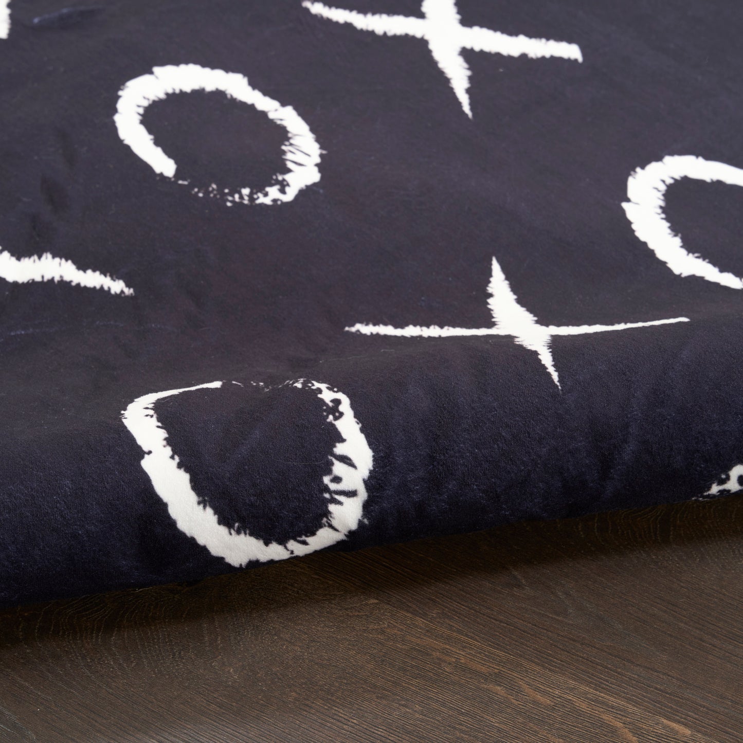 Dark navy throw blanket with white abstract brush-stroke shapes, draped over a wooden surface.