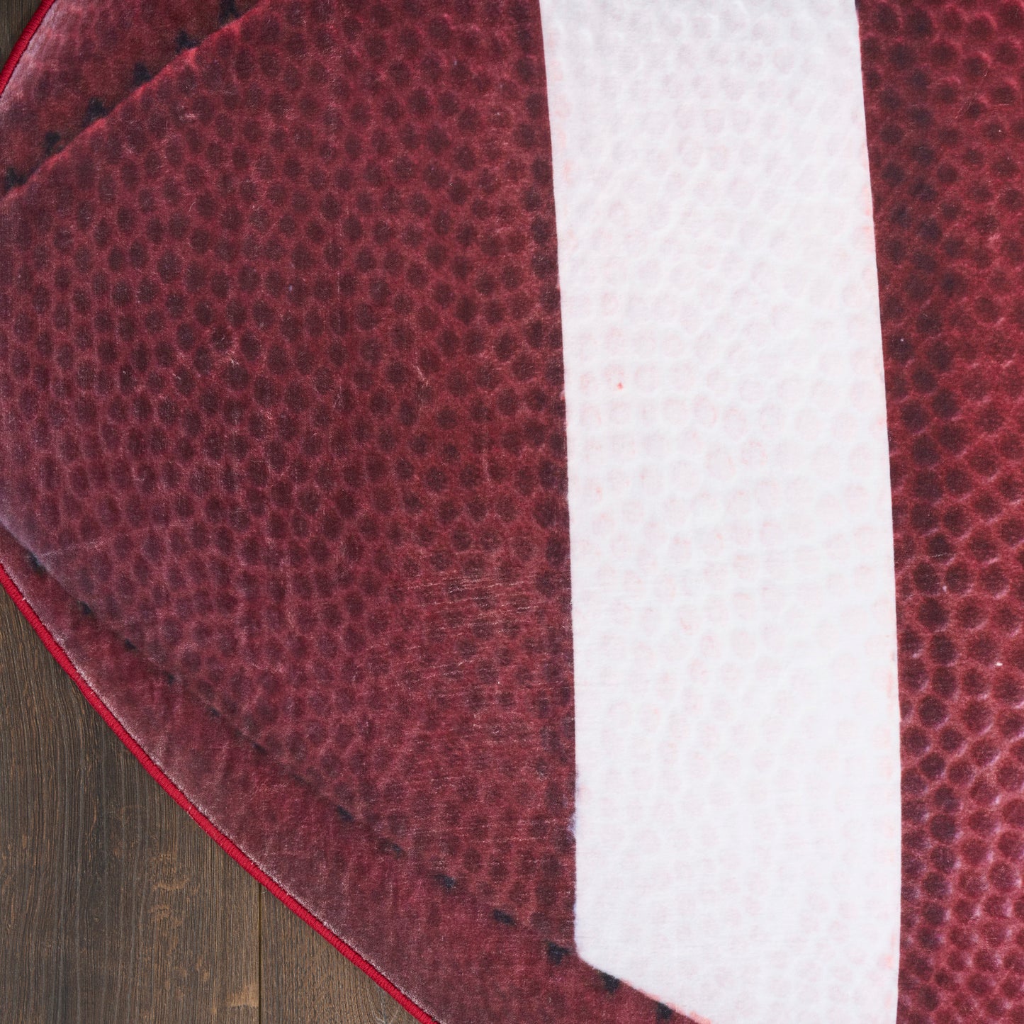 Close-up of burgundy pebbled leather with a white vertical stripe, curved edge, on a wooden floor.
