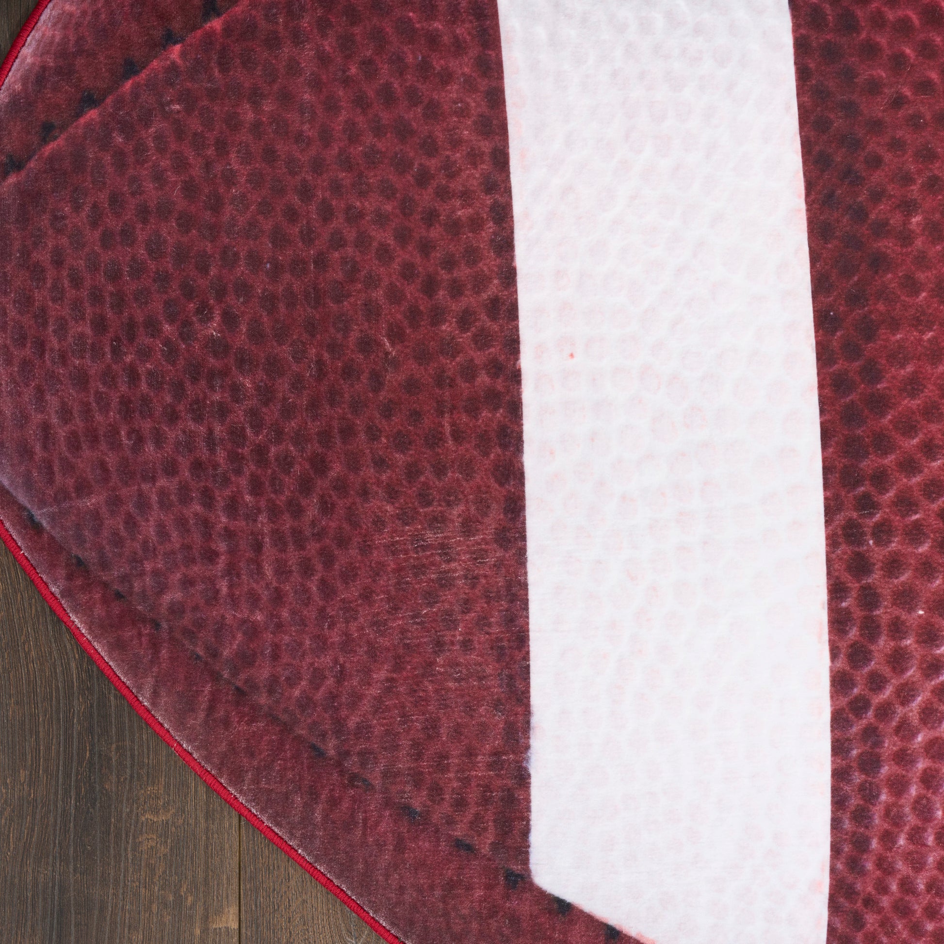 Close-up of burgundy pebbled leather with a white vertical stripe, curved edge, on a wooden floor.