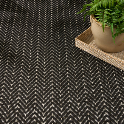 Black-and-beige chevron rug with a woven jute tray and potted fern for a natural, cozy decor look.