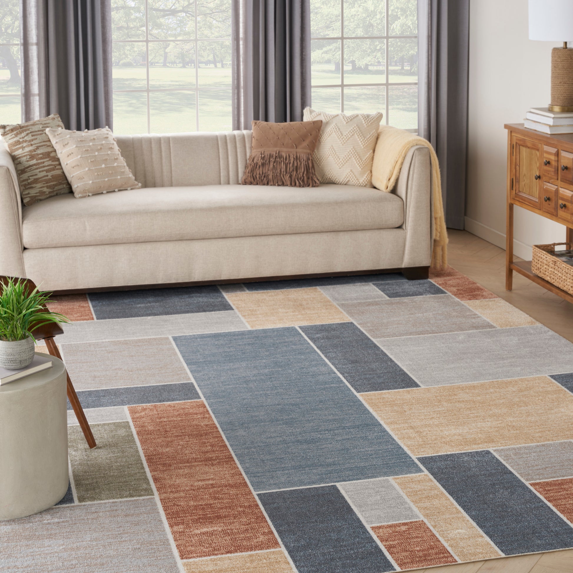 Geometric patchwork area rug in blue, beige, tan, and rust tones under a beige sofa.