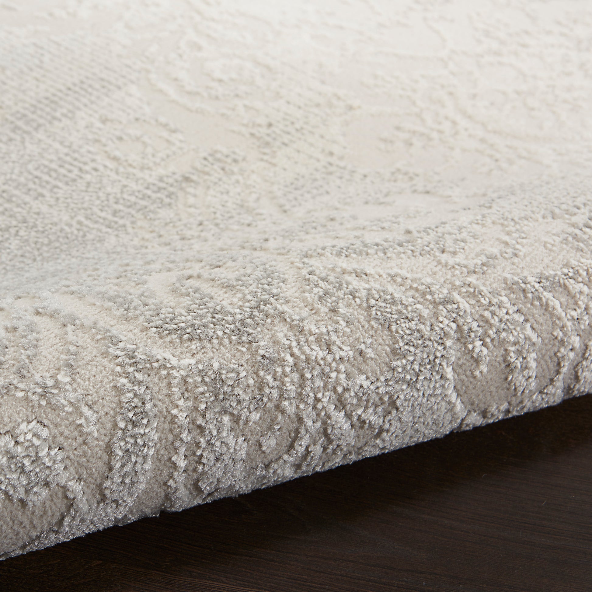 Cream beige textured rug close-up with a damask pattern and plush pile on dark hardwood floor.