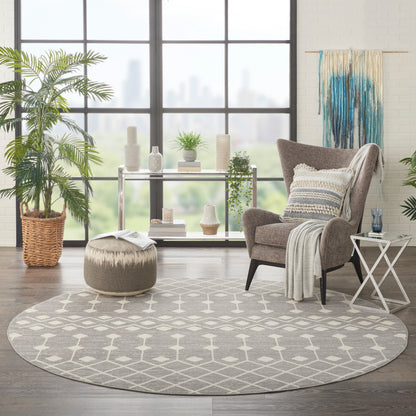 Circular gray geometric rug anchors a bright modern living room with a gray armchair, pouf, throw, plants, and large city-window view.