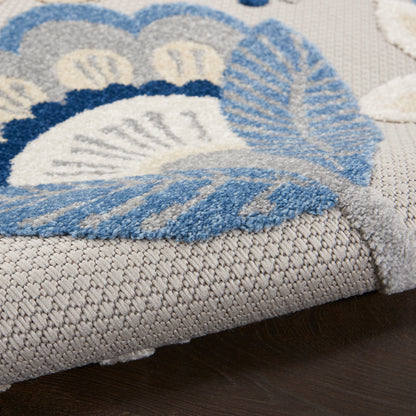 Soft plush rug in blue, gray and white with a floral pattern; thick pile and folded edge on dark wood floor.