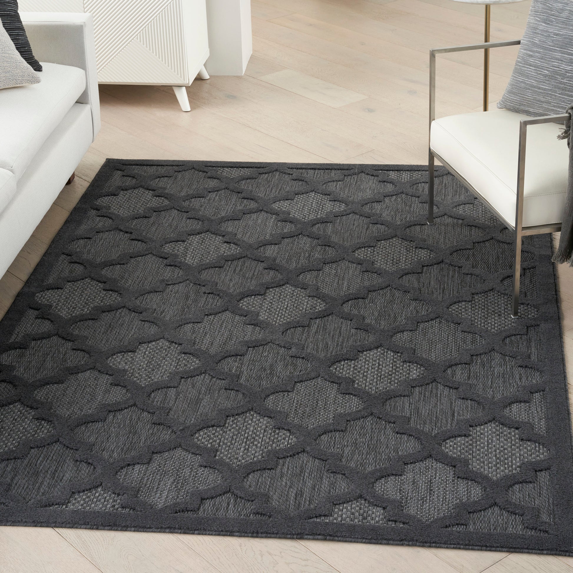 Dark gray geometric area rug with interlocking lattice/quatrefoil pattern on light wood floor in a modern living room.