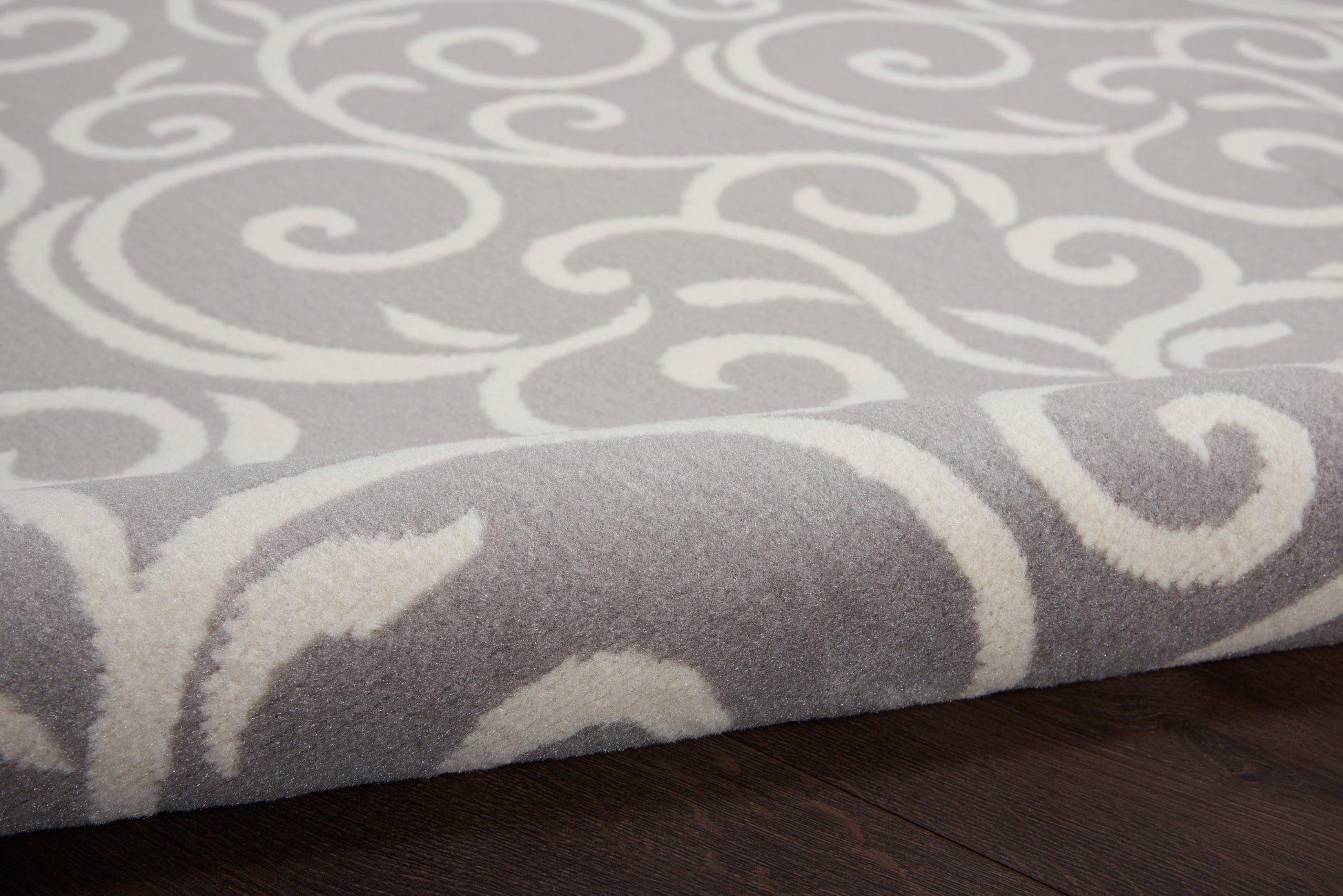 Soft grey rug with white scrolling swirl pattern, plush pile on dark wood floor