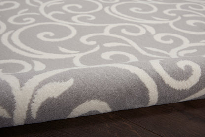 Soft grey rug with white scrolling swirl pattern, plush pile on dark wood floor