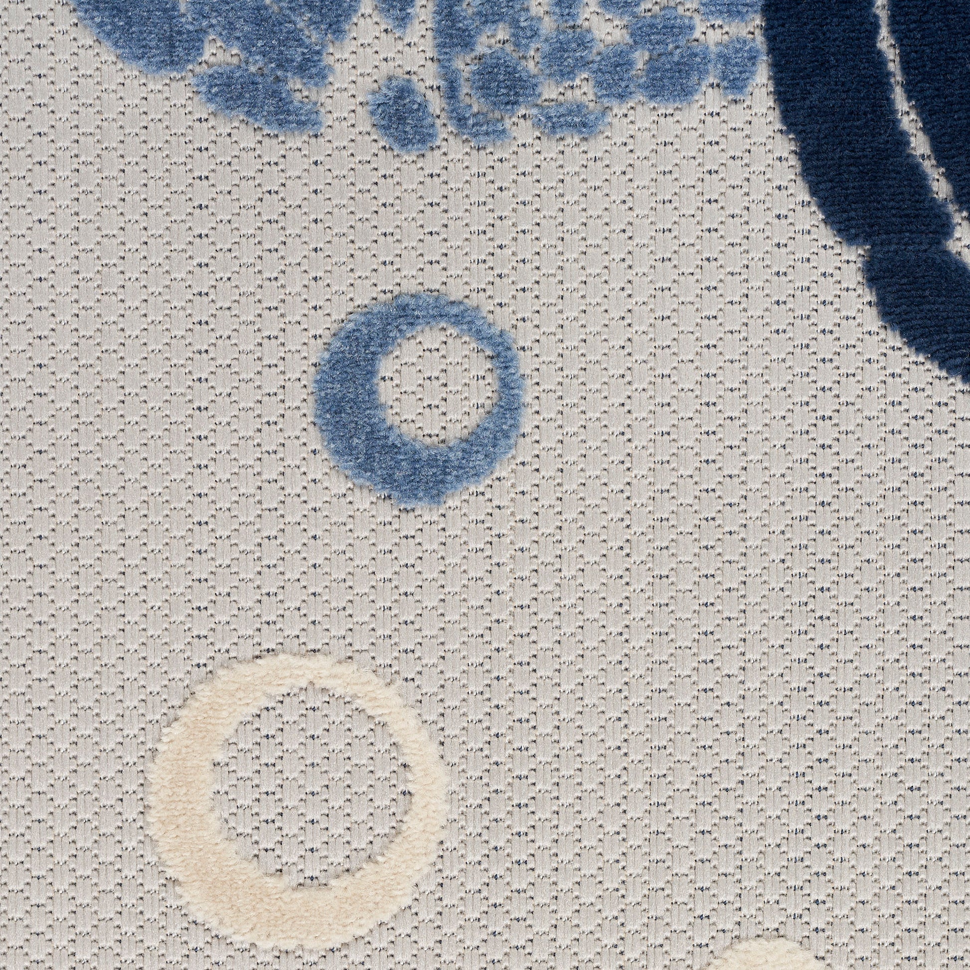 Beige woven rug with blue ring circles and partial blue floral motif; textured surface.