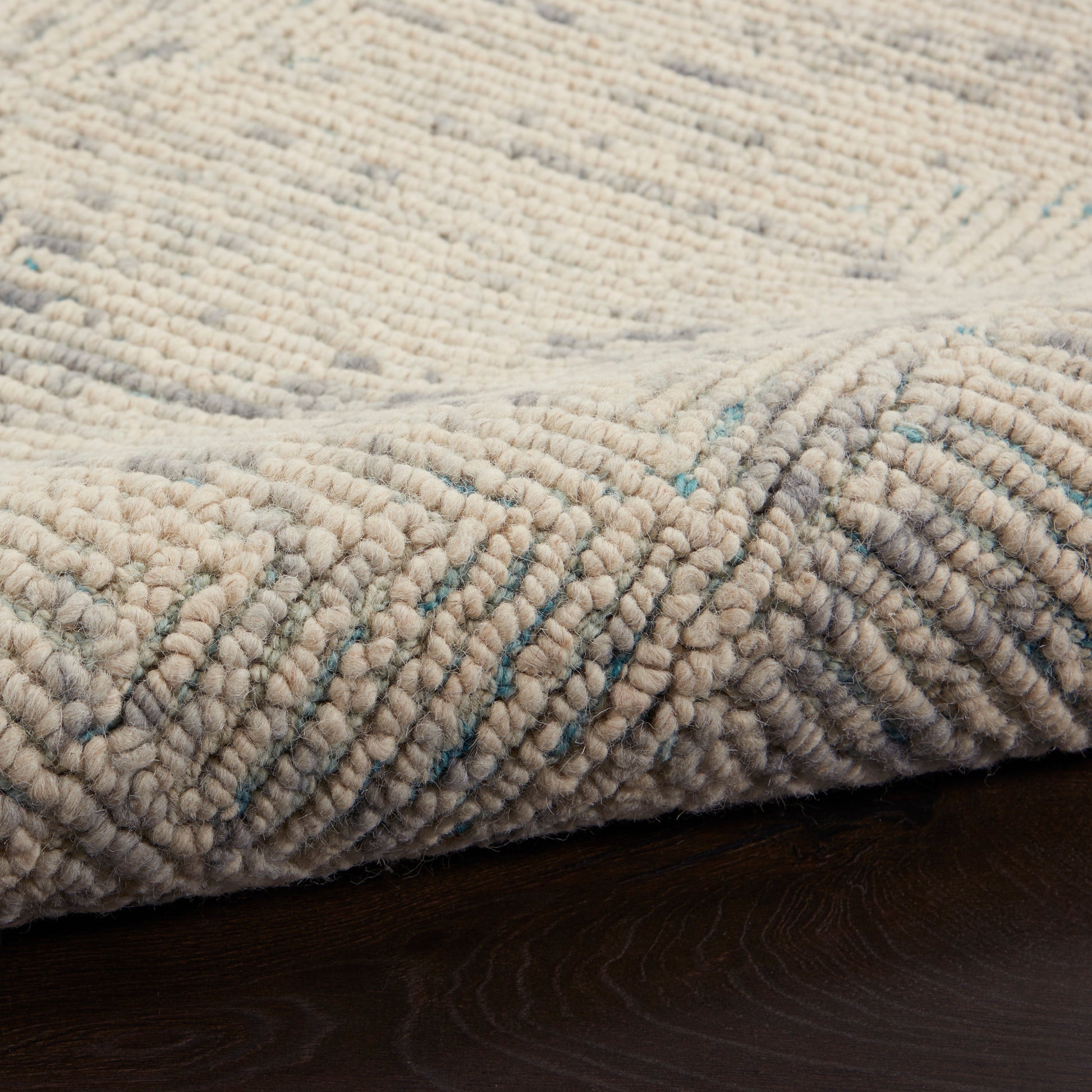 Beige textured loop rug with subtle teal flecks on dark wood floor, chunky soft pile, cozy contemporary style.