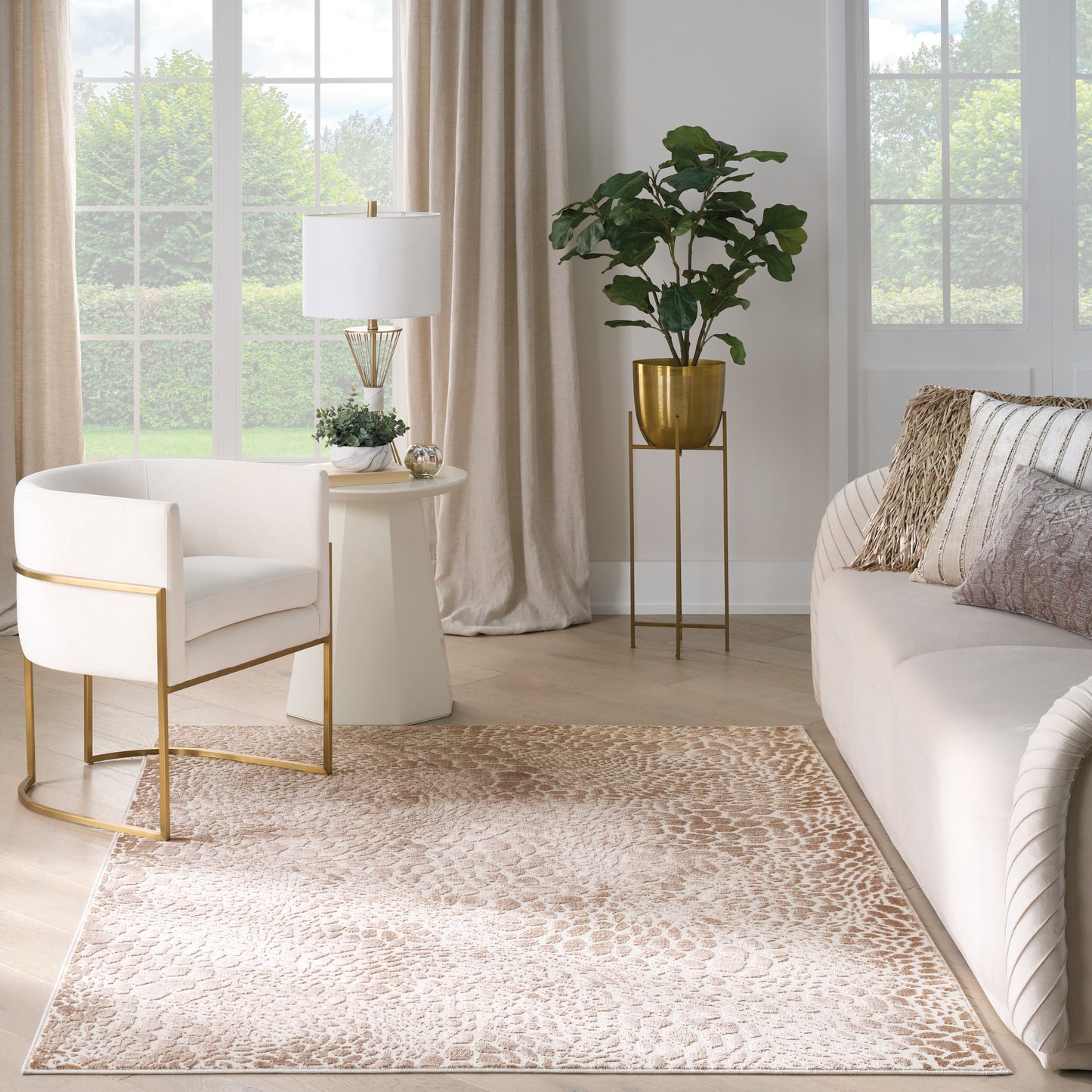 Neutral luxe living room with cream chairs, gold frames, round side table, beige rug, white sofa, potted plant on gold stand.