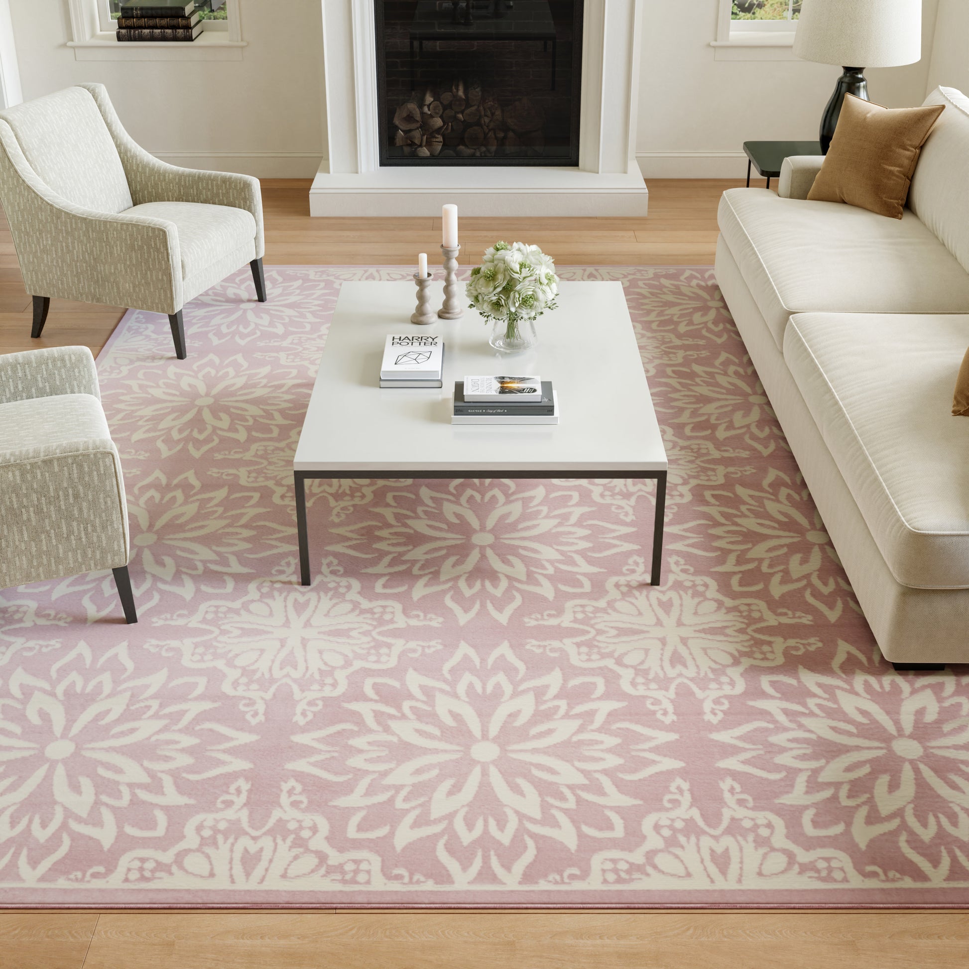 Cozy living room with pink floral rug, white coffee table, cream sofa and chairs, candles and flowers.