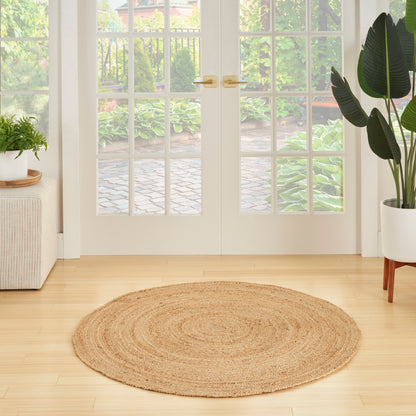Round natural jute rug on light wood floor in entryway with glass French doors, potted plants, bright airy decor.