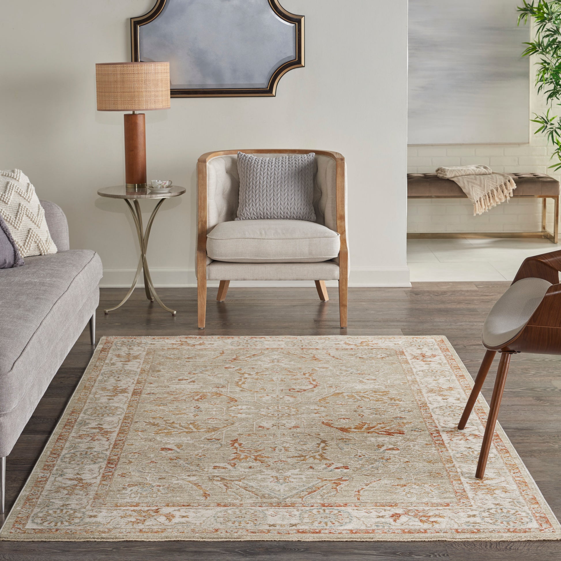 Cream oriental-pattern rug with peach accents in a neutral living room, wood-framed armchair, gray sofa, and round side table.