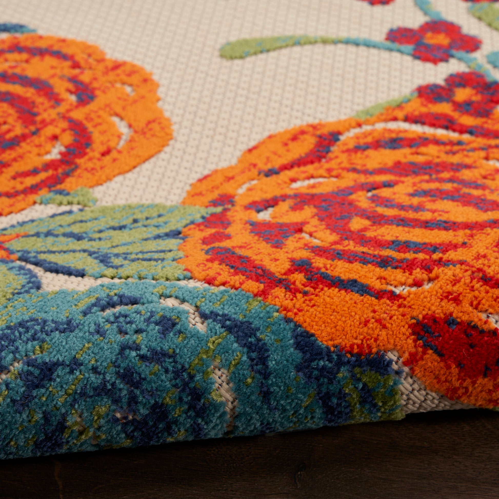Close-up of an outdoor floral rug with orange roses & blue-green leaves on a beige background, tufted with a thick pile.