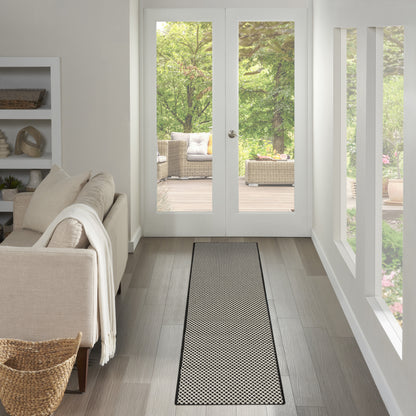 Geometric black-and-white rug runner on grey wood floor in a bright living room with beige sofa and glass doors to outdoors.