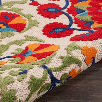 Beige woven rug with bold red, blue, orange and green floral pattern; traditional style, rolled edge on dark wood floor.