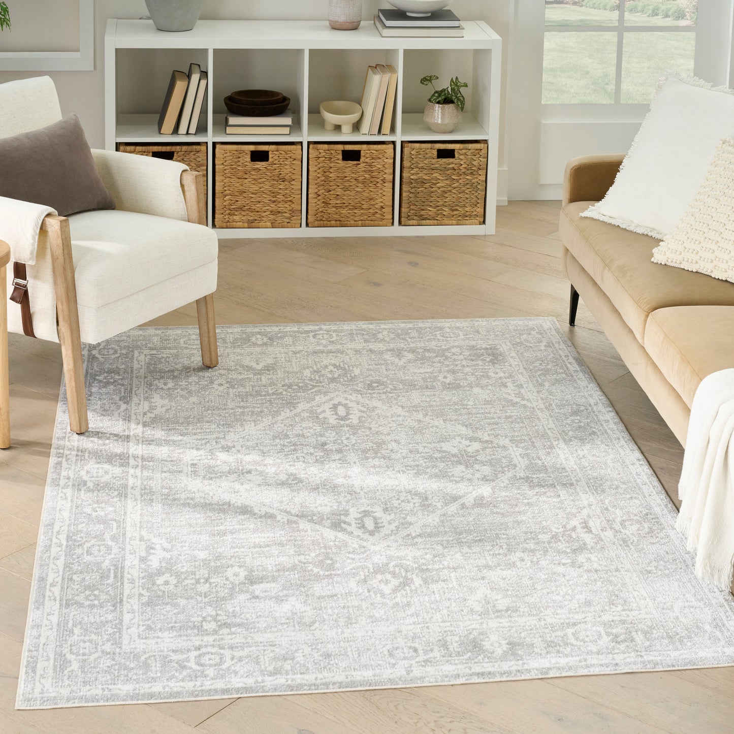 Soft gray patterned area rug on a light wood floor in a bright living room with white shelving and wicker baskets.