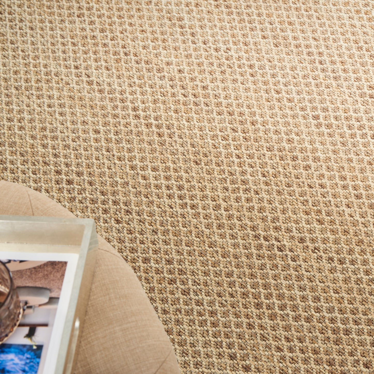 Beige woven textured rug with a round beige side table and a photo book on it.