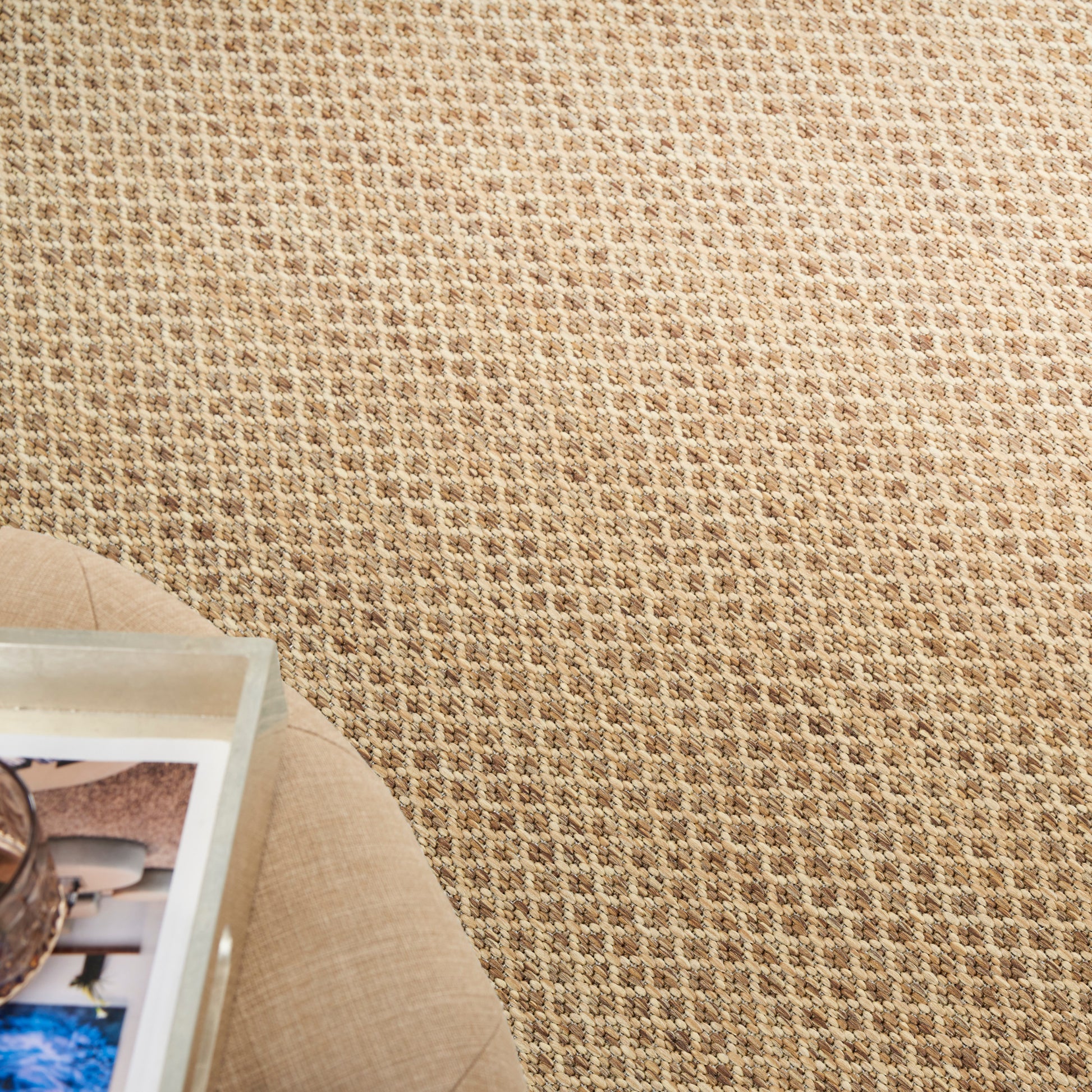 Beige woven textured rug with a round beige side table and a photo book on it.
