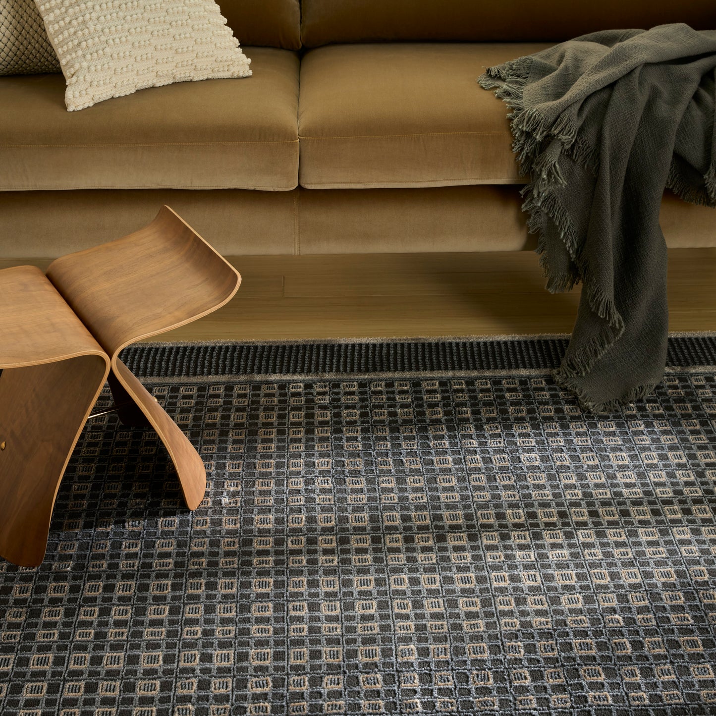 Beige fabric sofa with cream textured pillow, curved plywood side table, dark throw, on a grey geometric area rug.