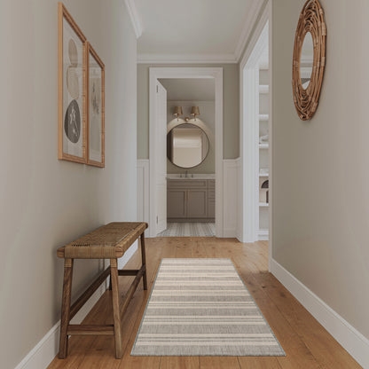 Neutral hallway with wooden bench, striped rug, round wicker mirror; opens to bathroom with round mirror above vanity.