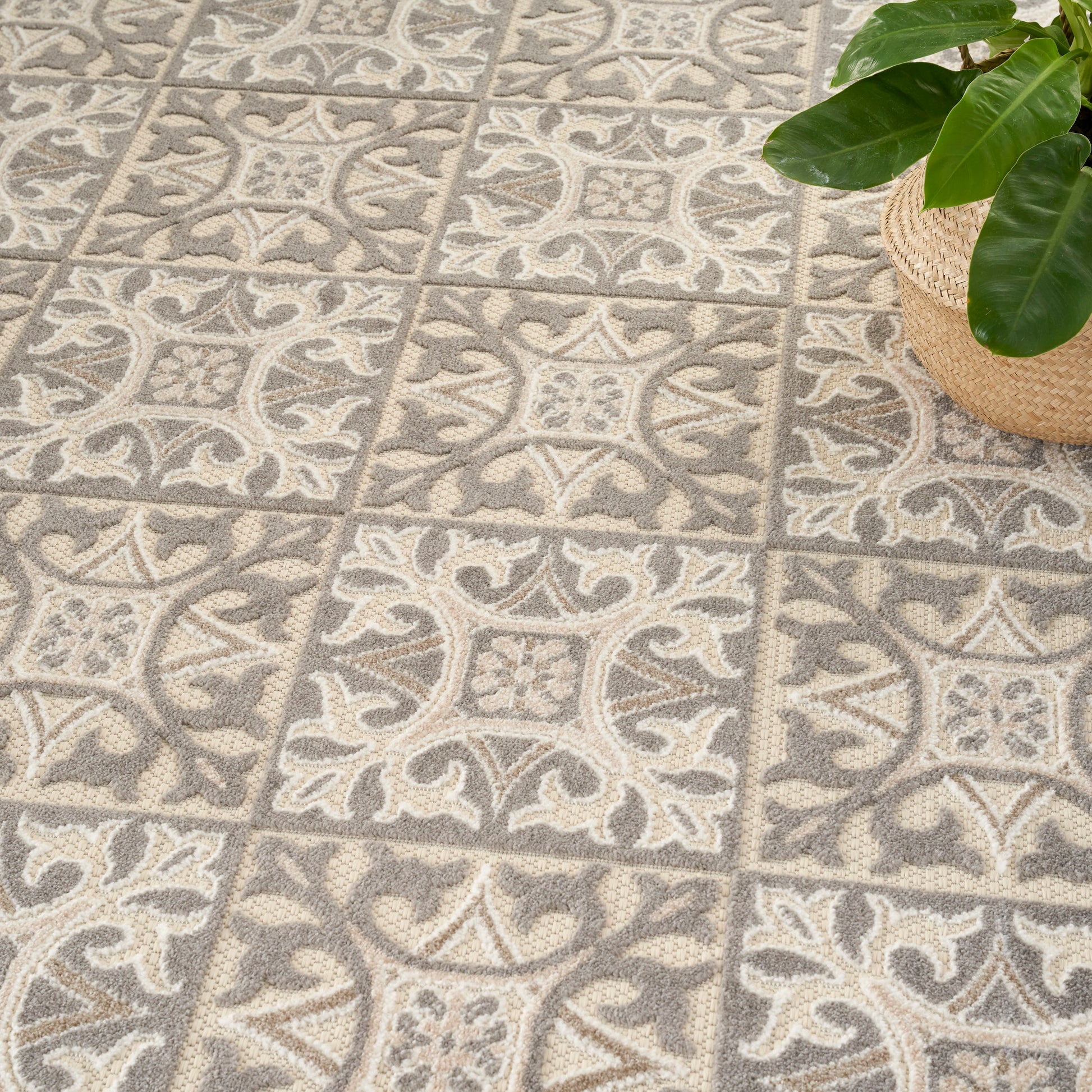 Grey & beige patterned rug with floral motifs in square blocks; a potted green plant in a woven basket in the corner.