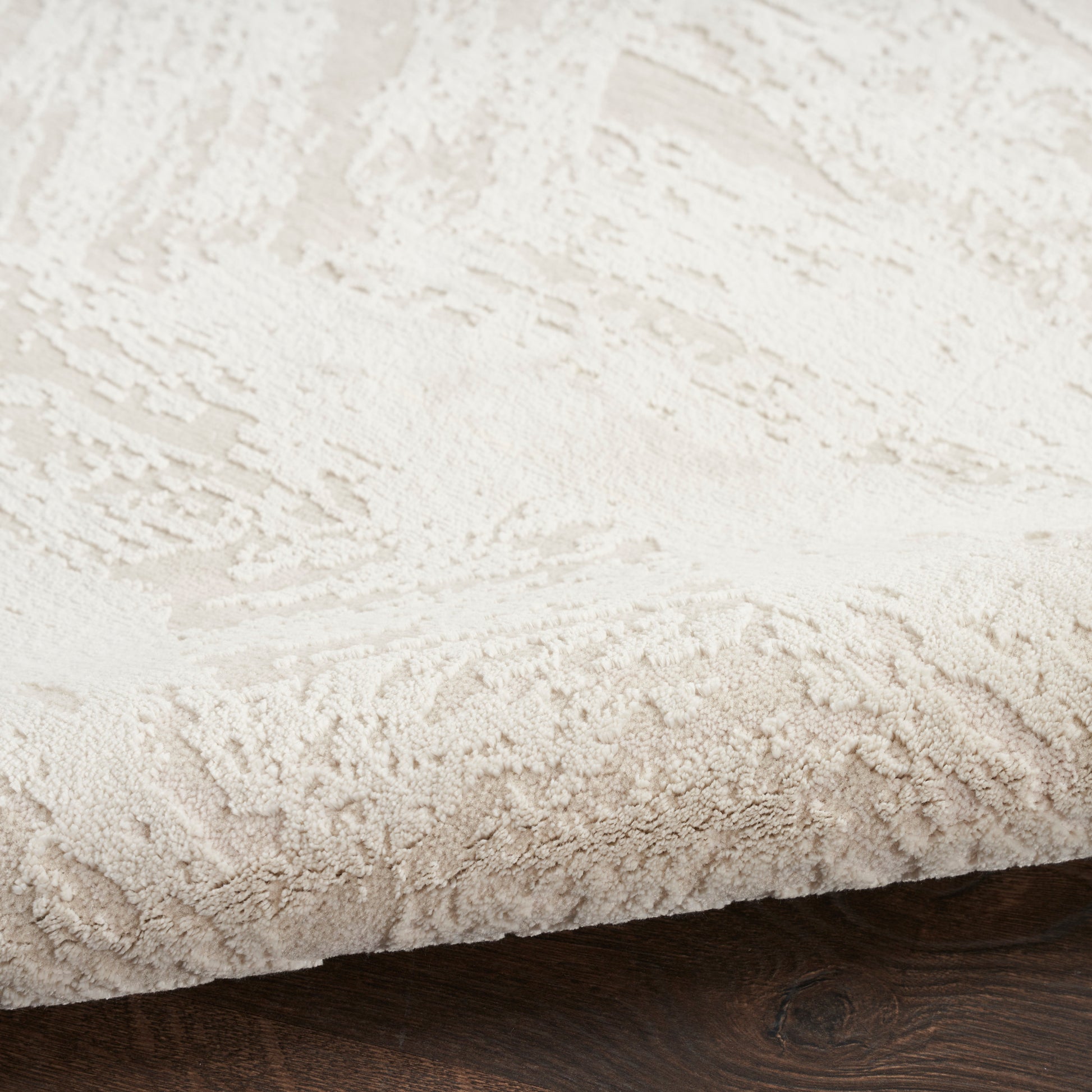 Beige rectangular shag rug with thick plush fibers and subtle pattern on dark hardwood floor.