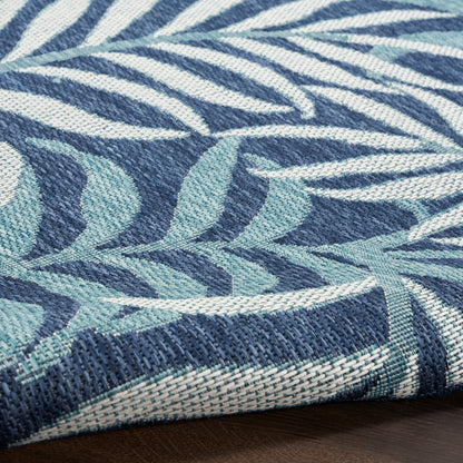Blue woven rug with teal tropical leaf pattern; textured navy and teal yarns, rolled edge visible.
